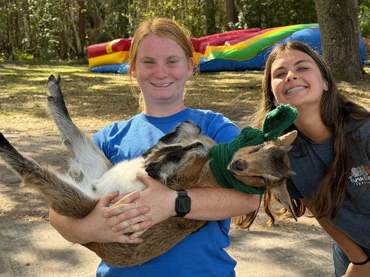 Two team members holding young goats in holiday scarves