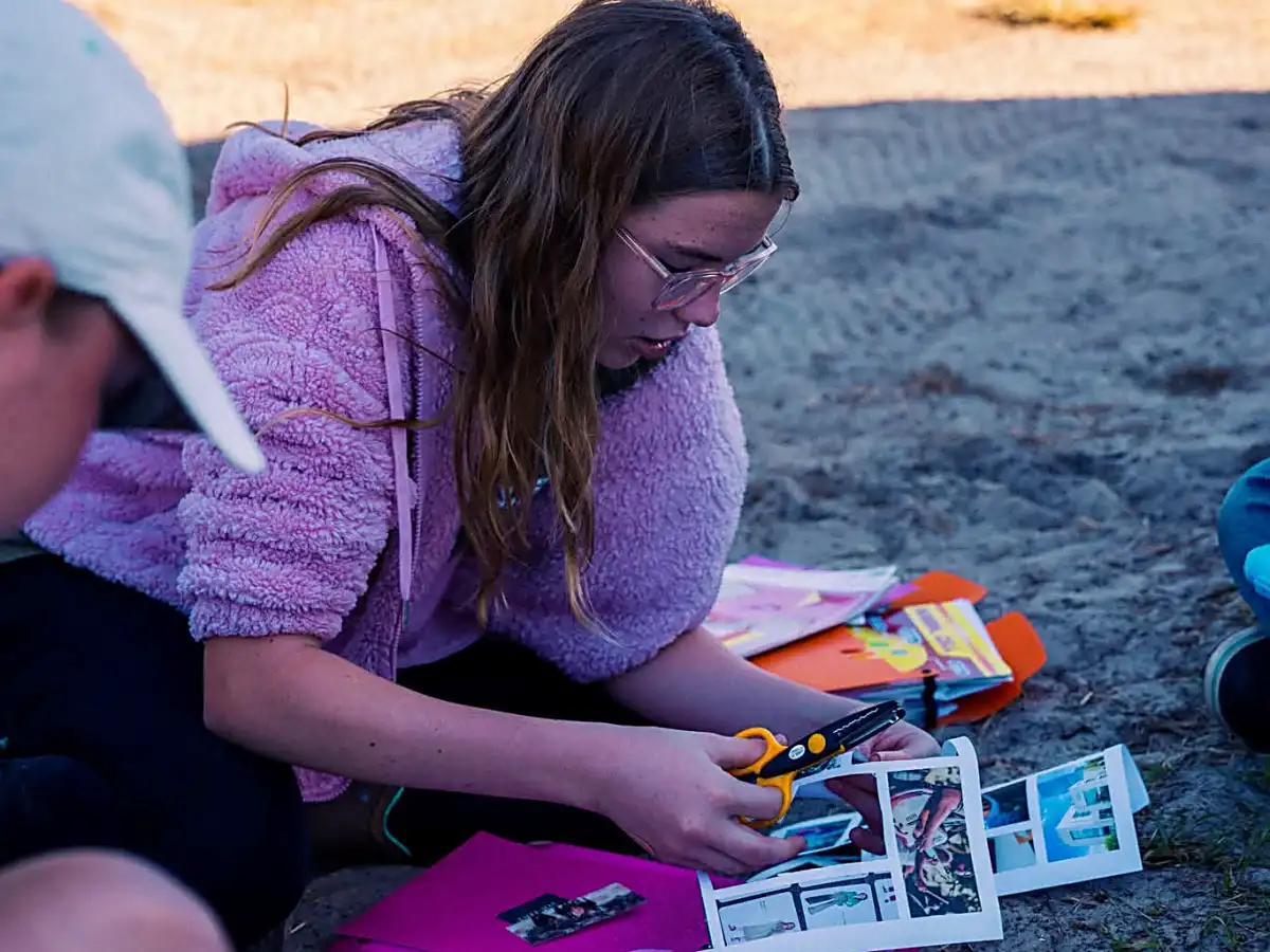 Student working on creative outdoor craft project with scissors and colorful materials